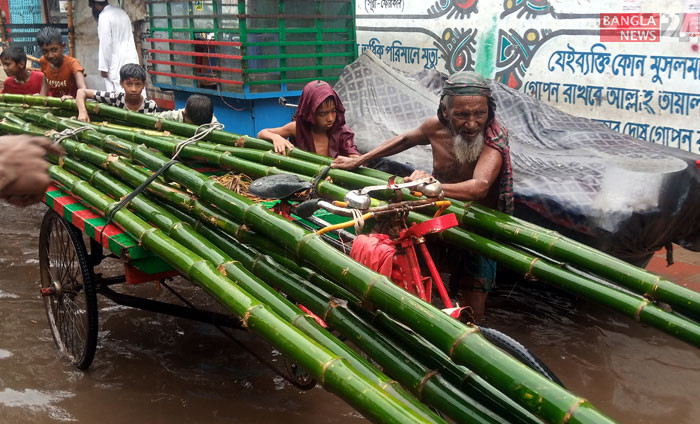 টানা বৃষ্টিতে কিছুটা স্বস্তি হলেও রাজধানীর বিভিন্ন সড়কে জলাবদ্ধতায় ভোগান্তিতে পড়েছেন পথচারীরা। জলাবদ্ধতার পানি মাড়িয়ে ভ্যানে করে ছোট শিশুদের সঙ্গে ঠেলে বাঁশ নিতে দেখা যায় এক বৃদ্ধকে। ছবি: আবাদুজ্জামান শিমুল